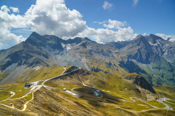 Austrian Alp mountain pass switchbacks Horizontal and downward wide angle view of an alpine road curving sharply over the surface of a green and yellow grass covered mountain in the foreground with a larger contrasting mountain range in the background.  Großglockner Hochalpenstrasse. grossglockner stock pictures, royalty-free photos & images