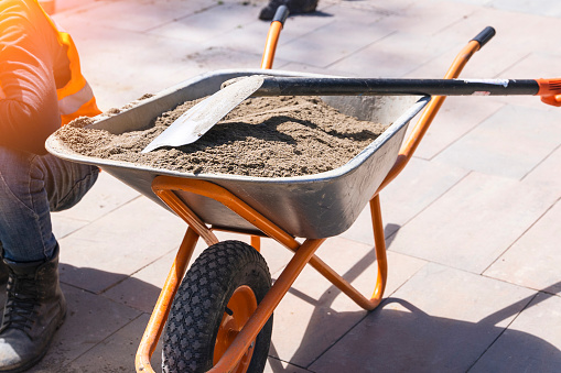 construction wheelbarrow with sand and shovel. A wheelbarrow full of sand on a construction site. a wheelbarrow on one wheel and a master worker