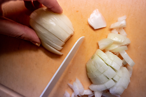 Women hands cutting onion in the kitchen close up, view from above