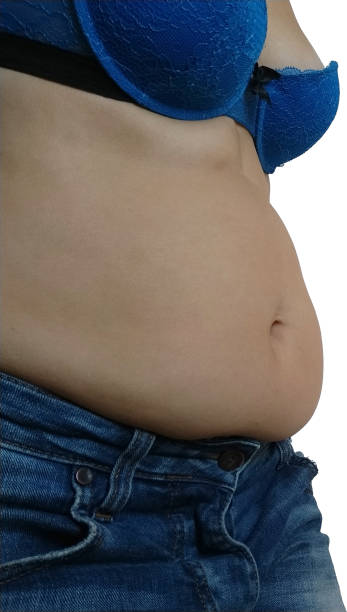 Saggy belly. Folds of leather and fat on the sides hanging over the waist of the jeans. A figure spoiled by overeating or pregnancy. Obesity and Diabetes. White background. Cellulite flabby muscles stock photo