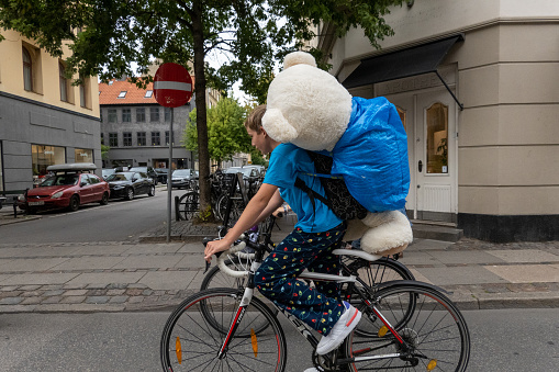 Copenhagen, Denmark  Sept 12, 2022 A young boy biking with a large teddy bear.