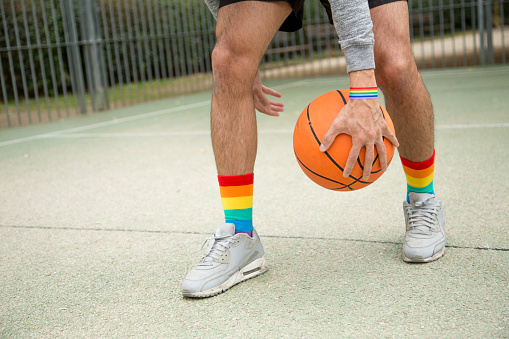 Basketball player in sneakers and rainbow socks dribbling with a ball in an outdoor court