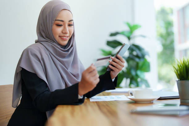 красивая мусульма�нка делает покупки в интернете с помощью телефона и кредитной карты - women middle eastern ethnicity islam hijab стоковые фото и изображения