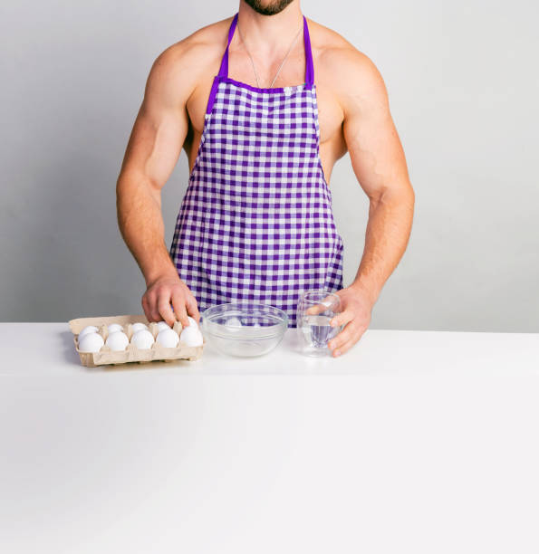 istock Chef bodybuilder in protective apron and cook eggs on whie kitchen table. Muscular man cooking. Healthy food and dieting. Food additives for sportsman, daily calorie diet 1432401608