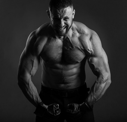 Studio portrait of fighting muscular man in black fighting gloves posing on dark background. The concept of mixed martial arts. Brutal bodybuilder energy and power boxing.