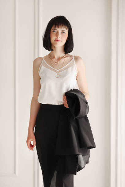 istock Confident young brunette business woman looking at camera on white wall background. Studio portrait of successful friendly female with short hair in black suit and white blouse with jacket on shoulder 1432405130