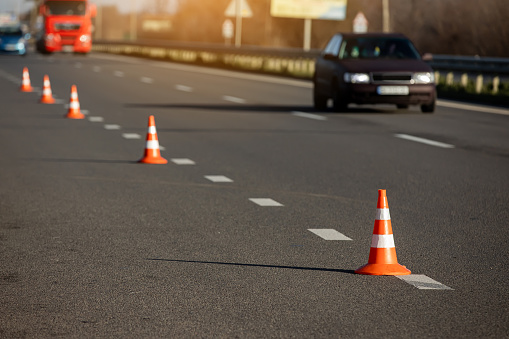 A row of traffic orange striped cones on the road. sunlight. These objects are temporary traffic control devices for directing and avoiding sections of the road being repaired or diverting traffic