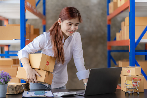 Asian business women, startups, SME entrepreneurs, check orders with computers, tablets and Packing items in shelf boxes with customers. Online Business Ideas and Freelance Jobs