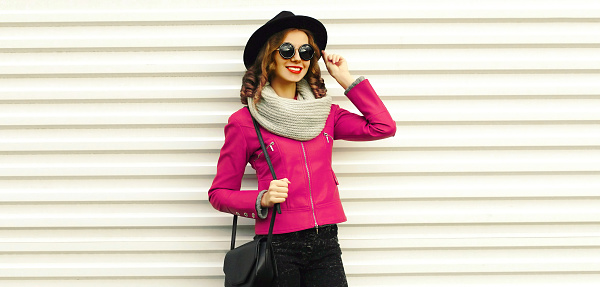 Portrait of beautiful smiling young woman wearing pink leather jacket, black round hat on white background