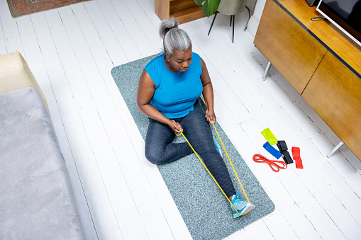 Mature black woman exercising at home using a resistance band - fitness concepts