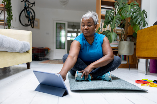 Senior woman doing her home workout following an online class using a tablet computer - healthy lifestyle concepts