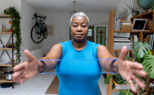 Portrait of a mature black woman exercising at home using a resistance band - healthy lifestyle concepts