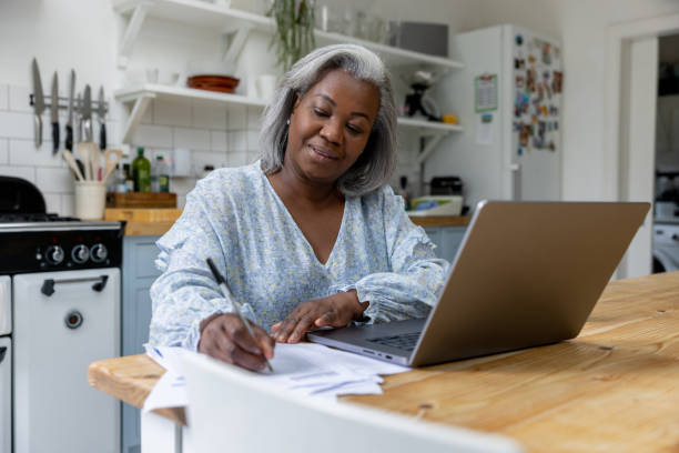 mulher madura em casa tendo aulas online usando seu laptop - uk check finance home finances - fotografias e filmes do acervo