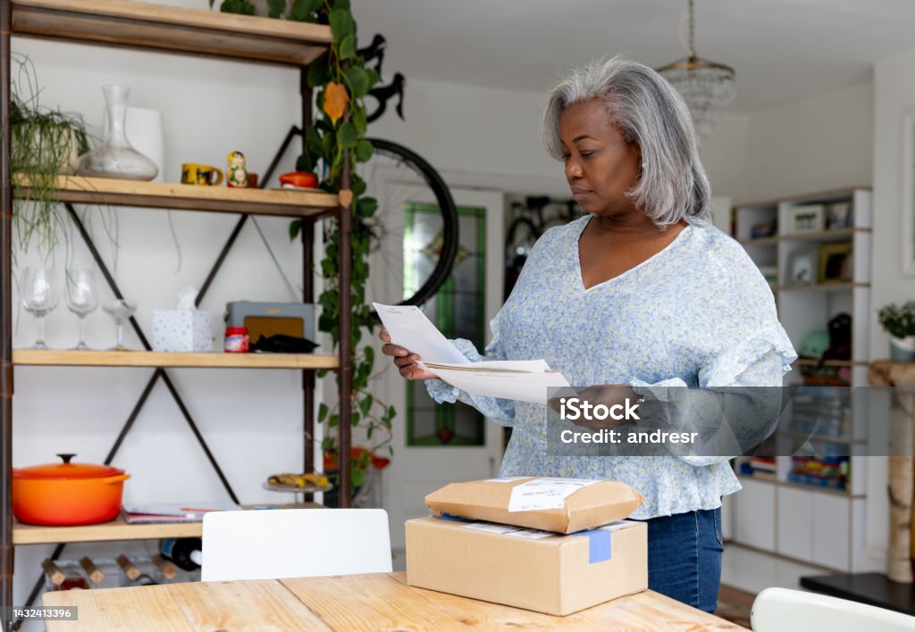 Woman at home checking her mail and reading a letter Mature black woman at home checking her mail and reading a letter - lifestyle concepts Mail Stock Photo