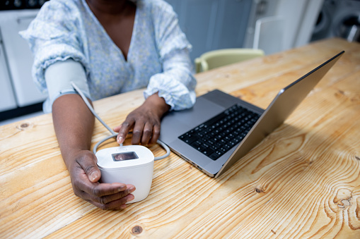 Close-up on a woman at home taking her blood pressure using a tensiometer while talking to a doctor on a video call