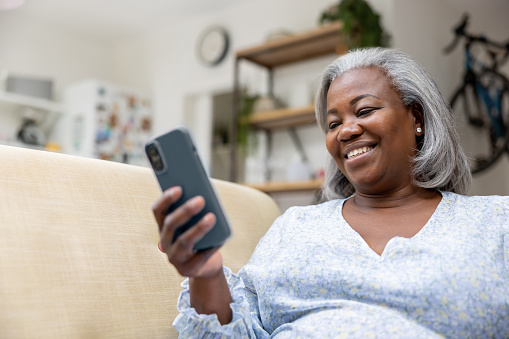 Mature woman at home looking happy watching videos on her cell phone and laughing - lifestyle concepts