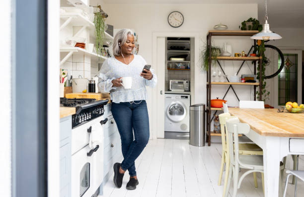 Woman at home watching videos on her cell phone Woman at home watching videos on her cell phone while drinking a cup of coffee and using headphones - lifestyle concepts britain british audio stock pictures, royalty-free photos & images