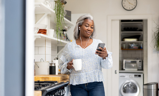Woman at home watching videos on her mobile phone while drinking a cup of coffee and using headphones - lifestyle concepts