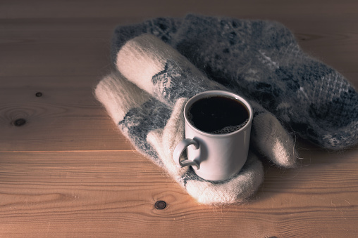 Cup of coffee and warm fluffy wool mittens on a wooden table.