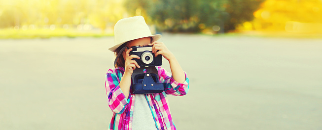 Portrait of child with film camera taking picture wearing summer straw hat on the city street