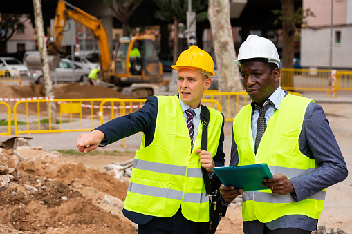 African-american and European men engineers discussing road repairing works. One engineer pointing with finger.