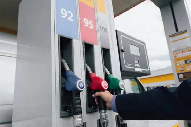 Photo of A businessman in a suit manages his car with gasoline at a gas station. Hand and red refueling gun close-up.