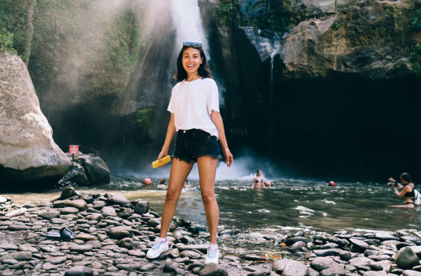 jeune femme joyeuse debout à côté de la cascade de montagne - hiking young women outdoors t shirt photos et images de collection
