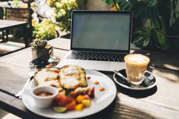 Modern netbook near glass with fresh coffee and delicious toasts on wooden table in terrace of cozy restaurant under sunlight