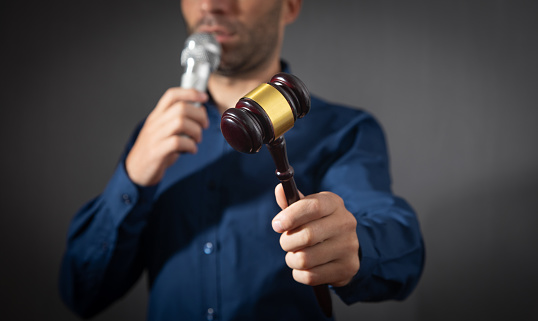 Caucasian auctioneer holding microphone and gavel.