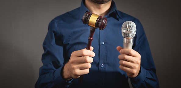 Caucasian auctioneer holding microphone and gavel.