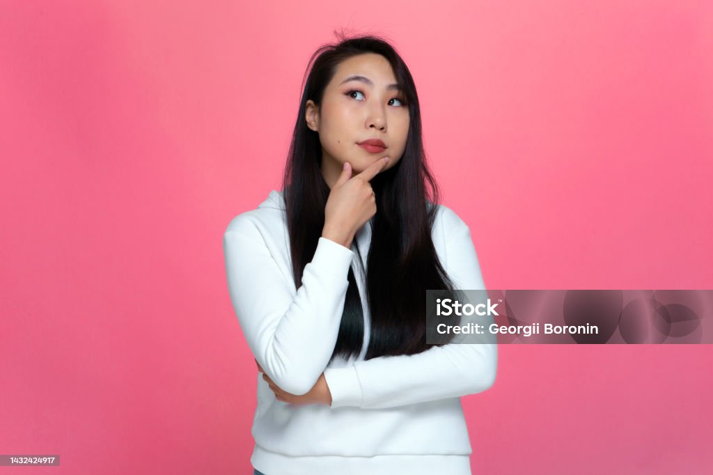 Pensive puzzled young asian girl looking up, considering problem solution, pondering decision on pink studio background Pensive puzzled young asian girl looking up, considering problem solution, pondering decision on pink studio background. High quality photo Decisions Stock Photo