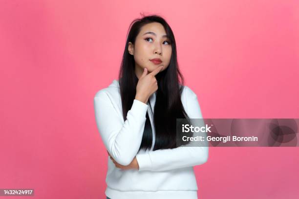 Pensive Puzzled Young Asian Girl Looking Up Considering Problem Solution Pondering Decision On Pink Studio Background Stock Photo - Download Image Now