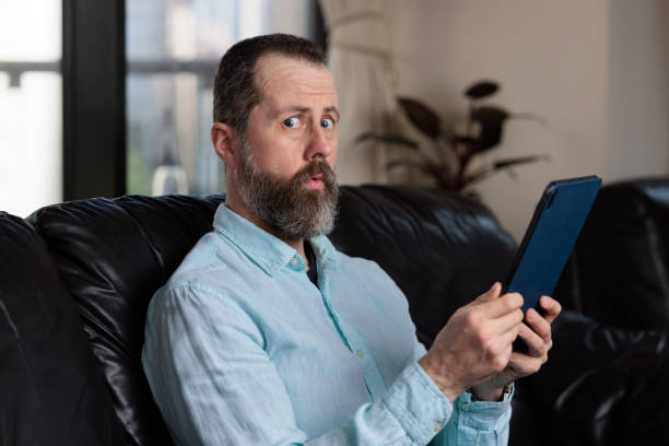 hombre preocupado con una tableta digital - levantando una ceja fotografías e imágenes de stock