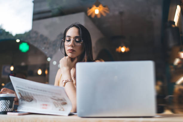 mujer concentrada con computadora portátil leyendo noticias - mujer leyendo periodico fotografías e imágenes de stock