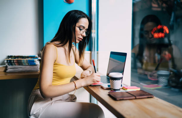 istock Skilled female copywriter in classic eyeglasses writing informative notes while connecting to 4g wireless internet on modern netbook computer, Caucaisan hipster girl in spectacles working remotely 1432426952