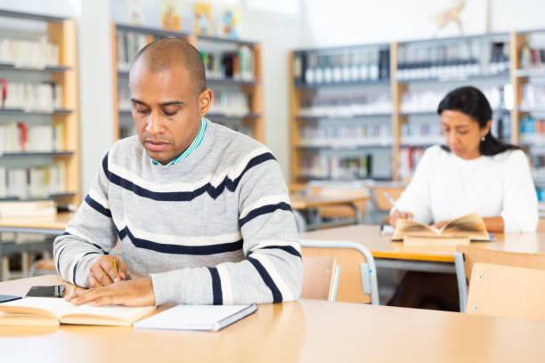 istock Adult hispanic man reading books and making notes in library 1432427994