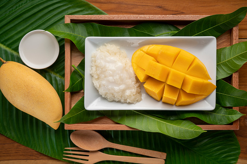 Sticky rice with mango and coconut milk on white plate over mango leaf, Sweet Mango Sticky Rice with Coconut Milk on white plate.
