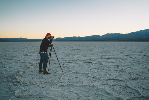 Full length of focused male photographer standing on salt flats of Badwater Basin located in USA and taking shot of majestic scenery in evening