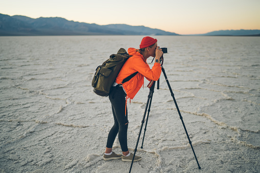 Side view of unrecognizable female explorer using photo camera on tripod while standing on salt flats during vacation in USA