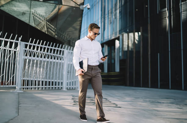 istock Trendy dressed businessman using modern mobile gadget for chatting with financial partners, Caucasian male manager walking and connecting to wireless on cellphone for installing banking application 1432429174