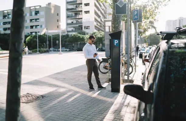 Photo of Caucasian businessman ticketing in parking meter during time in financial district of megalopolis, formally dressed male manager checking security payment via credit card at terminal machine