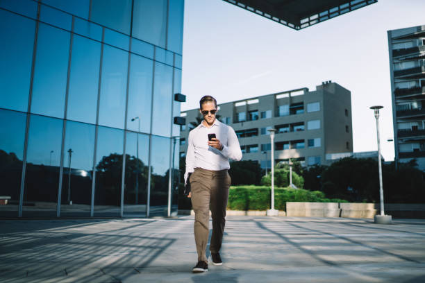 istock Trendy dressed young businessman making web booking via smartphone platform for online banking, handsome male manager walking and connecting to wireless on cellphone for searching financial news 1432429192