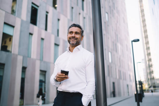 istock Happy professional employee with modern mobile phone smiling at urban setting in downtown, successful entrepreneur holding smartphone device enjoying business lifestyle in financial district 1432429256