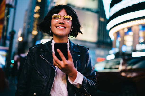 istock Cheerful millennial blogger with modern cellphone technology for web chatting recreating at urban street, happy generation z in electronic headphones listening positive music playlist and smiling 1432429393