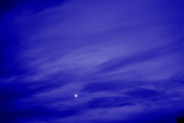 Waxing crescent moon shining in a twilight sky over a dark hillside