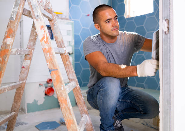 The technology of laying tile, repair and decoration. Focused man puts porcelain tiles on wall sitting squat at bathroom stock photo