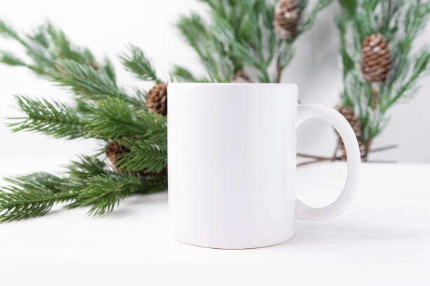 istock White ceramic cup with space for text or logo on a wooden table with Christmas tree branches in the background. 1432432518