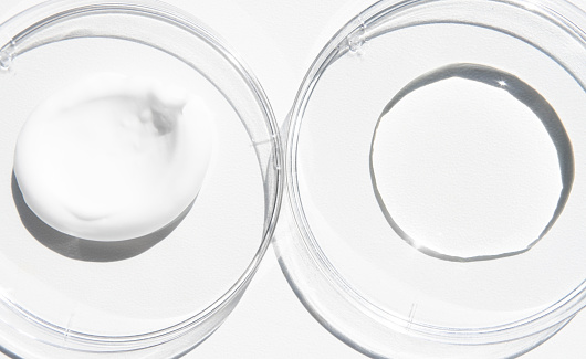 Cosmetic texture close-up on a white background with bright light. Liquid transparent hyaluronic acid and white body care cream in a glass container