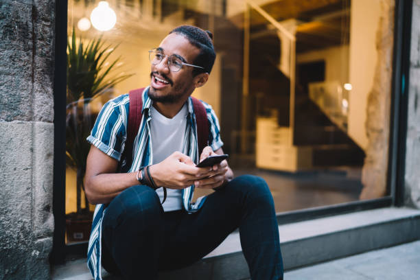 istock Positive happy dark skinned hipster guy in eyewear looking away using smartphone for communicating on free time in city, cheerful african american male holding mobile phone for browsing on leisure 1432433761