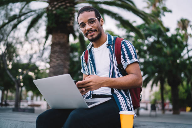 istock Portrait of positive dark skinned male it developer enjoying working outdoors using 4G connection and laptop computer, millennial african american student browse information for online education 1432433781
